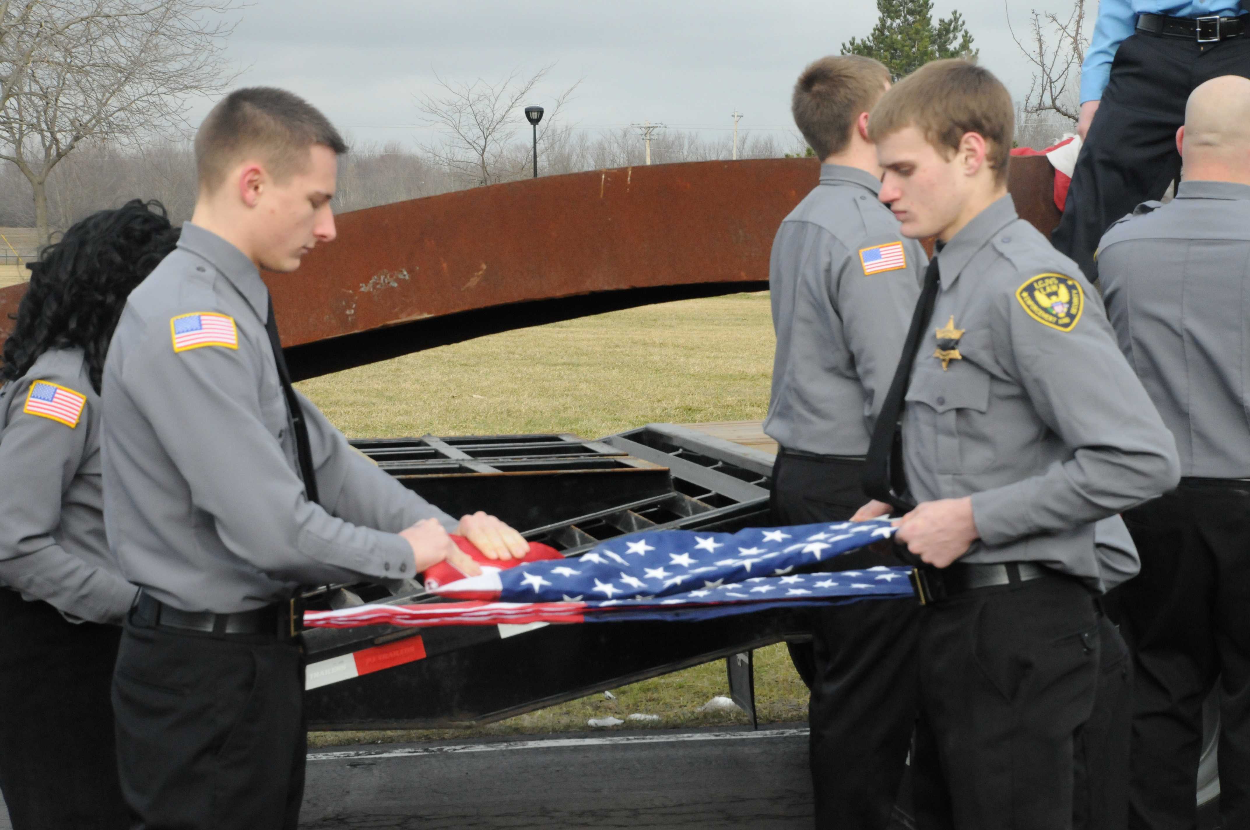 two male student fold American flag taken from beam